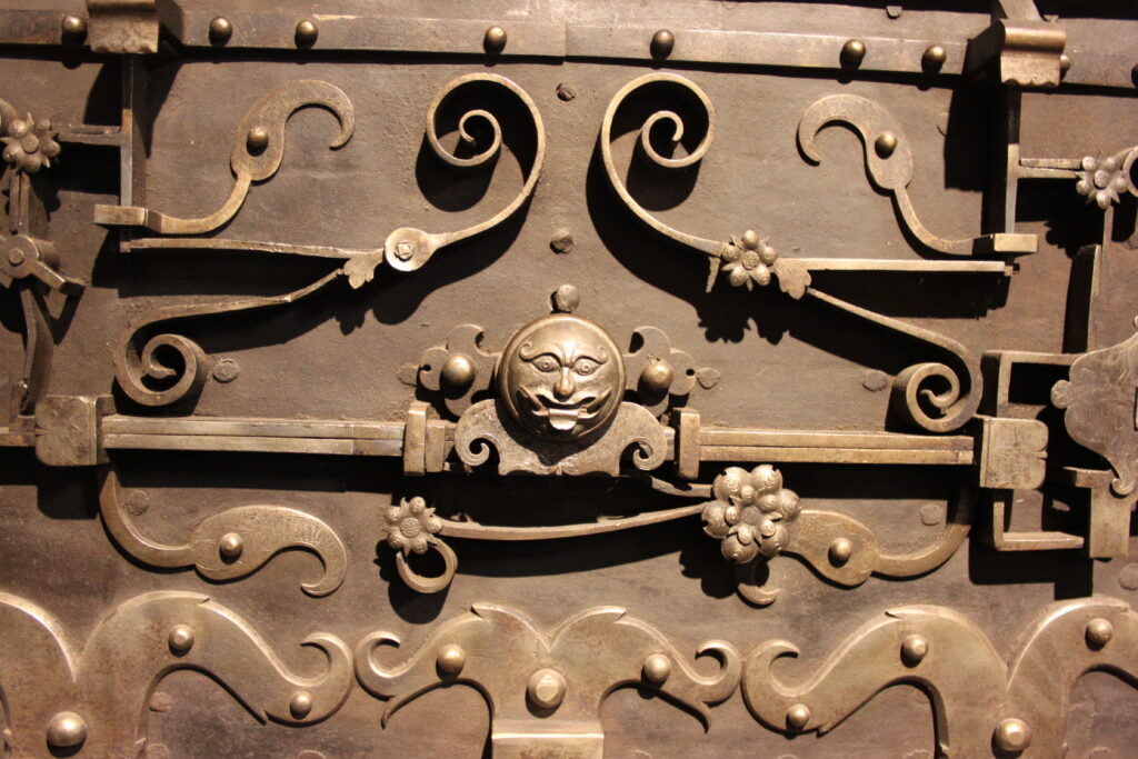 Detailansicht einer kunstvoll verzierten Metallbeschläge mit floralen Mustern und einem zentralen Gesichtsmotiv.