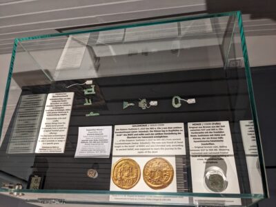 In einer Vitrine sind verschiedene historische Münzen und Objekte aus Gold und Silber ausgestellt.
