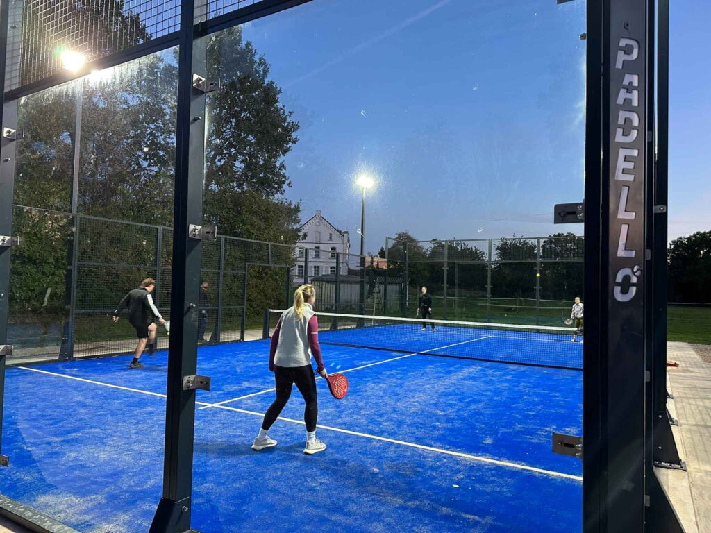 Zwei Personen spielen Padel in einem beleuchteten Außenplatz während der Dämmerung.