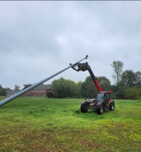 Ein Traktor mit einer großen Hebevorrichtung steht auf einer grünen Wiese unter bewölktem Himmel.